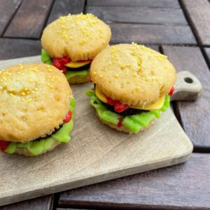 Drie cupcakes versierd als kleine hamburgers, met groene toef, gele ‘kaas’ en rode ‘saus’.