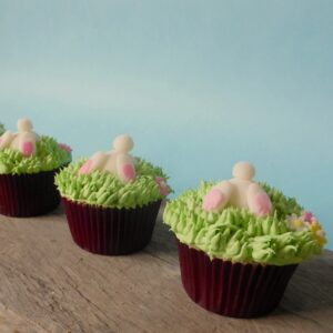 Cupcakes met witte konijntjes die met hun kontjes omhoog uit groen gras steken, op een houten tafel.